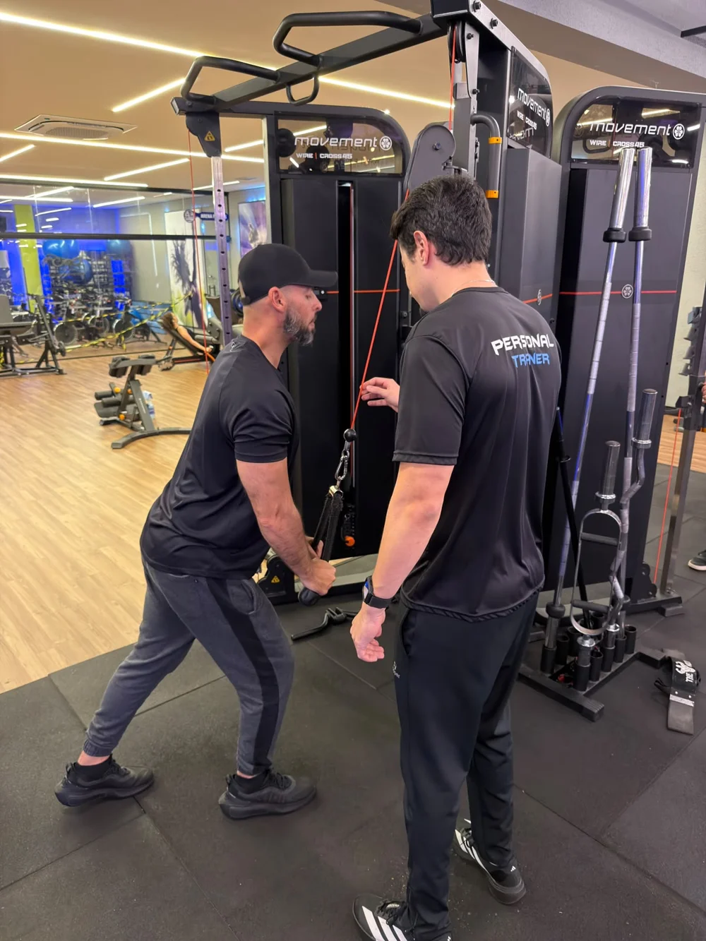 Vitor acompanhando um aluno no exercício de tríceps na polia